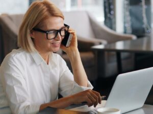 a woman talking on a cell phone while using a laptop