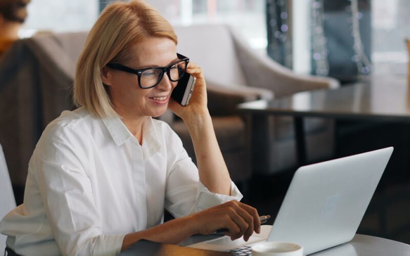 a woman talking on a cell phone while using a laptop