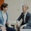 Three professionals in business attire conversing indoors.