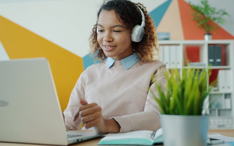 Young woman wearing headphones works on laptop.