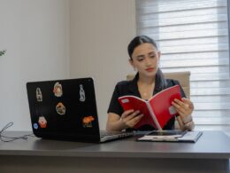 A woman reading a red book at a desk.